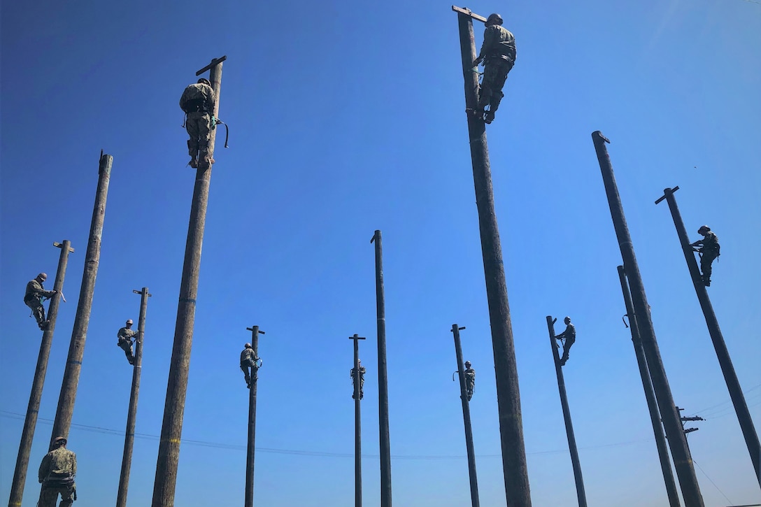 Navy Seabees practice working high above ground on utility poles.