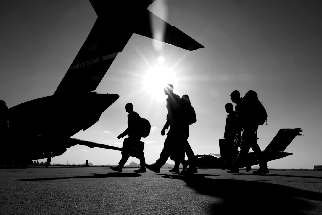 Airmen, shown in silhouette, walk toward an aircraft on a flightline.