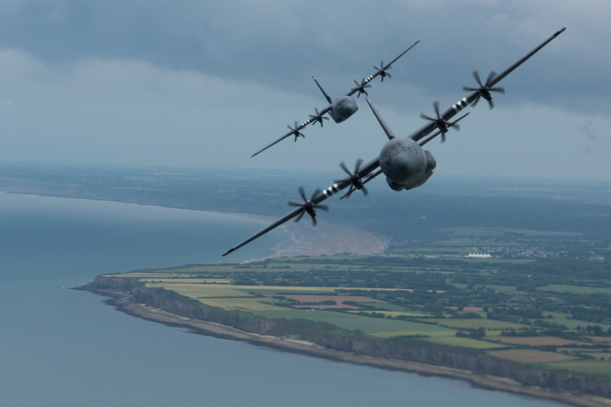 Two C-130J Super Hercules, belonging to the 37th Airlift Squadron on Ramstein Air Base, fly over Pointe-du-Hoc as part of a four-ship formation with a C-17 Globemaster III trailing a mile behind the formation in Normandy, France, June 5, 2019. Pointe-du-Hoc, coastal land featuring a 100 foot cliff overlooking the Atlantic Ocean, provided the highest vantage point between the American landing sectors at Utah and Omaha Beach on D-Day, June 6, 1944. The German army heavily fortified Pointe-du-Hoc as a result. Axis defenses notwithstanding, the U.S. Army Ranger Assault Group scaled the 100 foot cliff and soon after captured Pointe-du-Hoc. (U.S. Air Force photo by Senior Airman Kristof J. Rixmann)