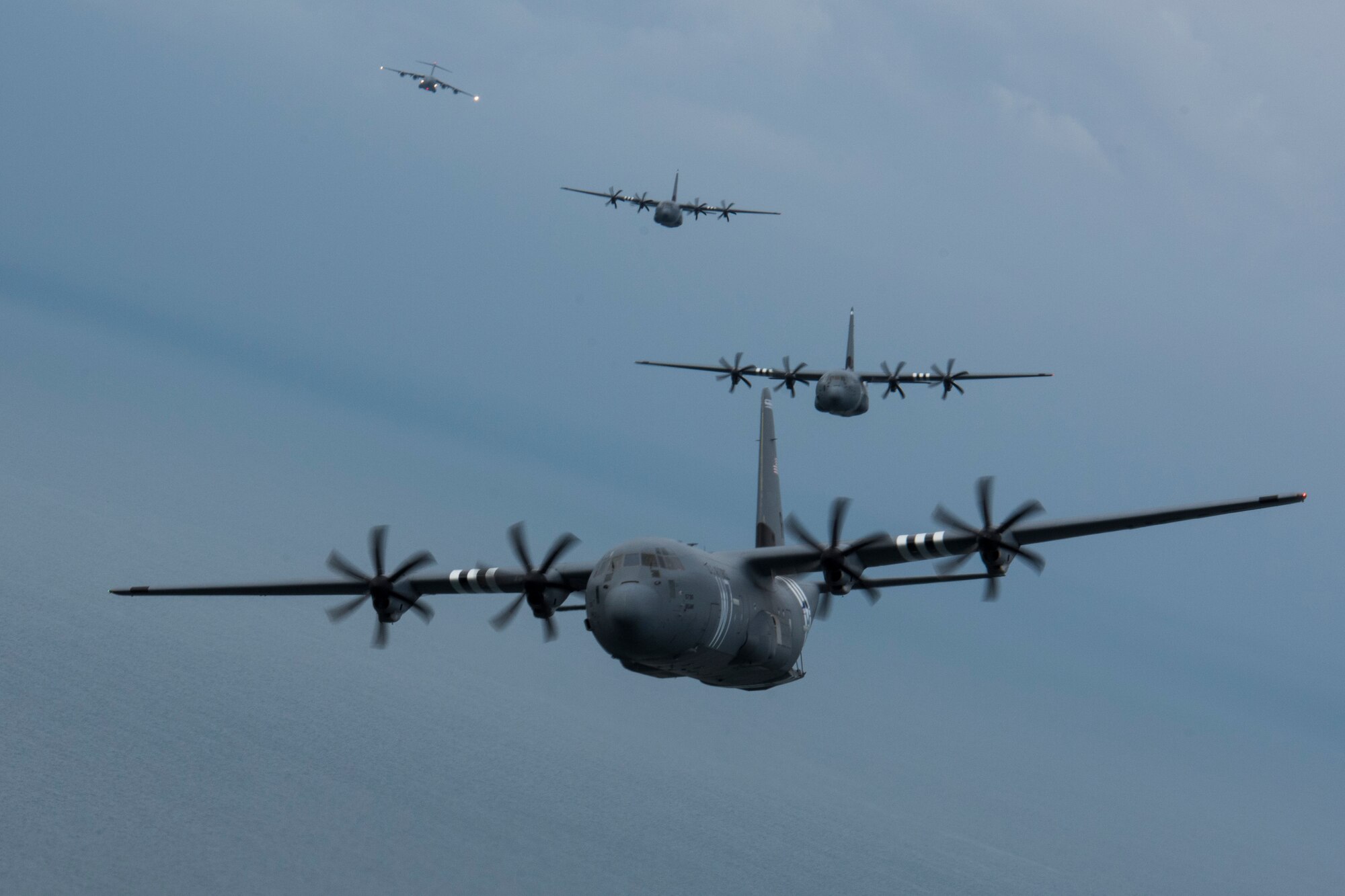 Three C-130J Super Hercules, belonging to the 37th Airlift Squadron on Ramstein Air Base, fly in a four-ship formation with a C-17 Globemaster III trailing a mile behind over the Atlantic Ocean near Normandy, France, June 5, 2019. The 37th AS is a legacy squadron to the 37th Troop Carrier Squadron, who on D-Day, June 6, 1944, accurately dropped hundreds of paratroopers onto the intended drop zone. The objective: to seize the city of Sainte-Mère-Église. The precision and accuracy carried out by the 37th TCS allowed the paratroopers to quickly take the city. Later, it would be discovered Sainte-Mère-Église was the first city liberated in France by Allied forces, in part because of the effort provided by the 37th TCS. (U.S. Air Force photo by Senior Airman Kristof J. Rixmann)
