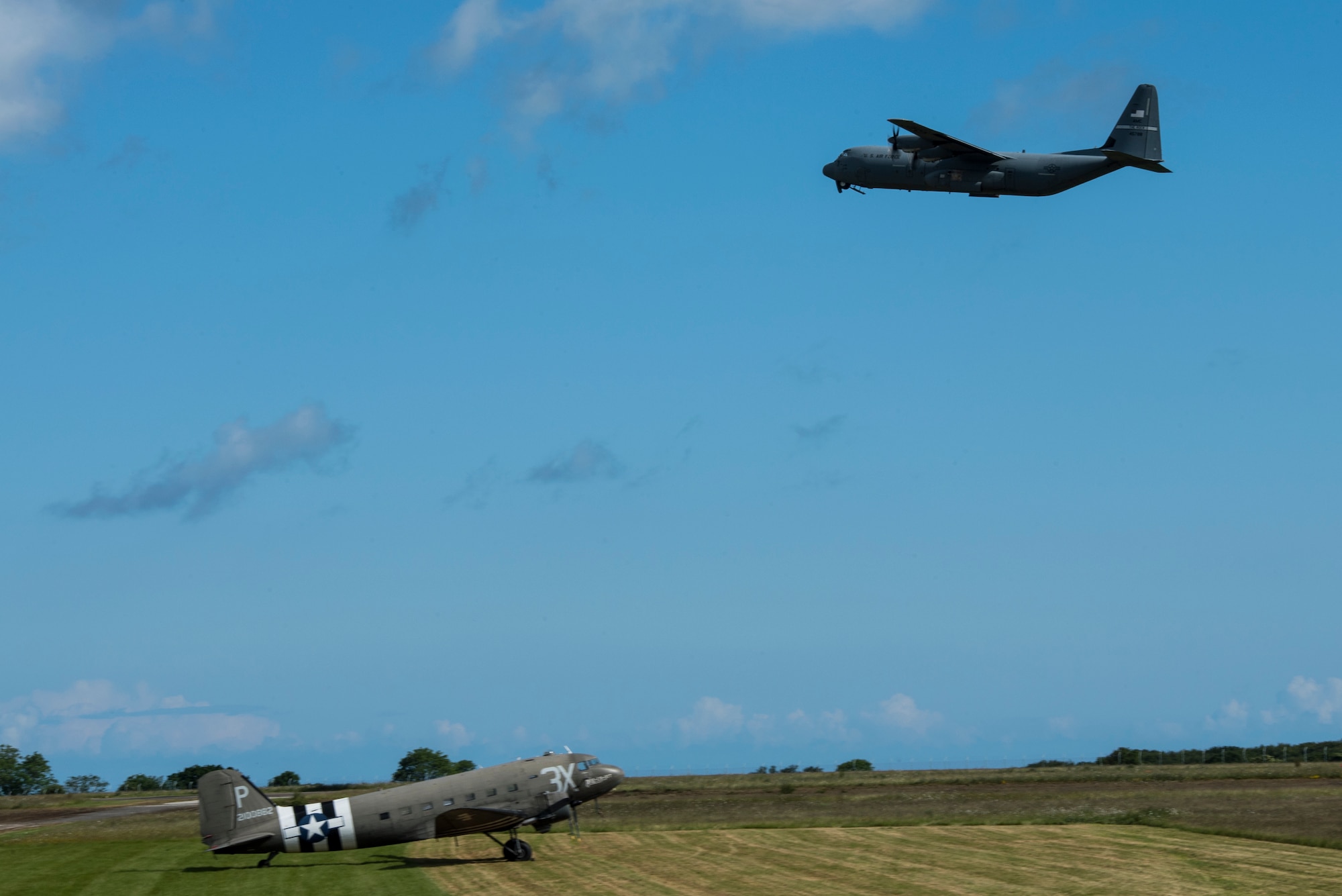 A U.S. Air Force C-130J Super Hercules, assigned to the 61st Airlift Squadron, Little Rock Air Force Base, Ark., flies over a Douglas C-47 Dakota at Cherbourg-Maupertus Airport, France, June 6, 2019. The 61st AS, draws lineage from the 61st Troop Carrier Squadron, which flew C-47s during the invasion of Normandy, 75 years ago. (U.S. Air Force photo by Senior Airman Devin M. Rumbaugh)
