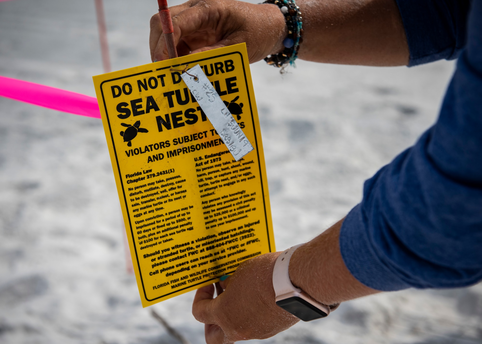 Rebecca Johnson, Tyndall Natural Resources wildlife and biological technician, hangs a warning sign on a barrier created around a sea turtle nest on the beach at Tyndall Air Force Base, Florida, June 5, 2019.