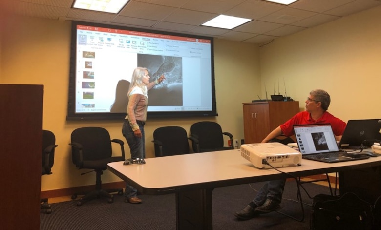 Woman on the left pointing at a screen and man on the right looking at presentation