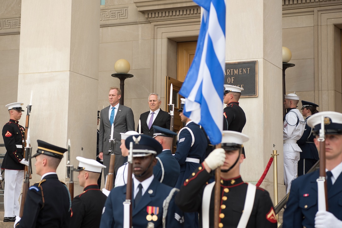 Acting Defense Secretary Patrick M. Shanahan and a Greek leader look out from a stairway at the entrance to a building as service members stand at attention.