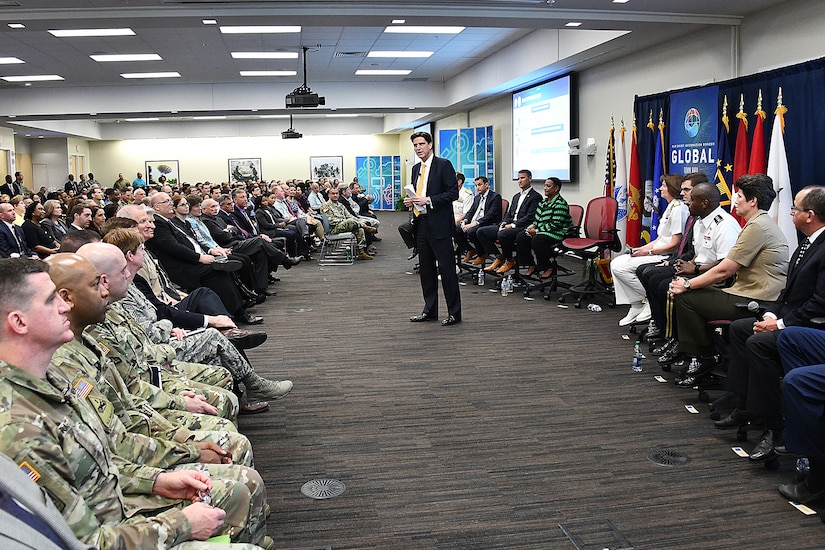 Man speaks to a conference room full of military and civilian personnel.