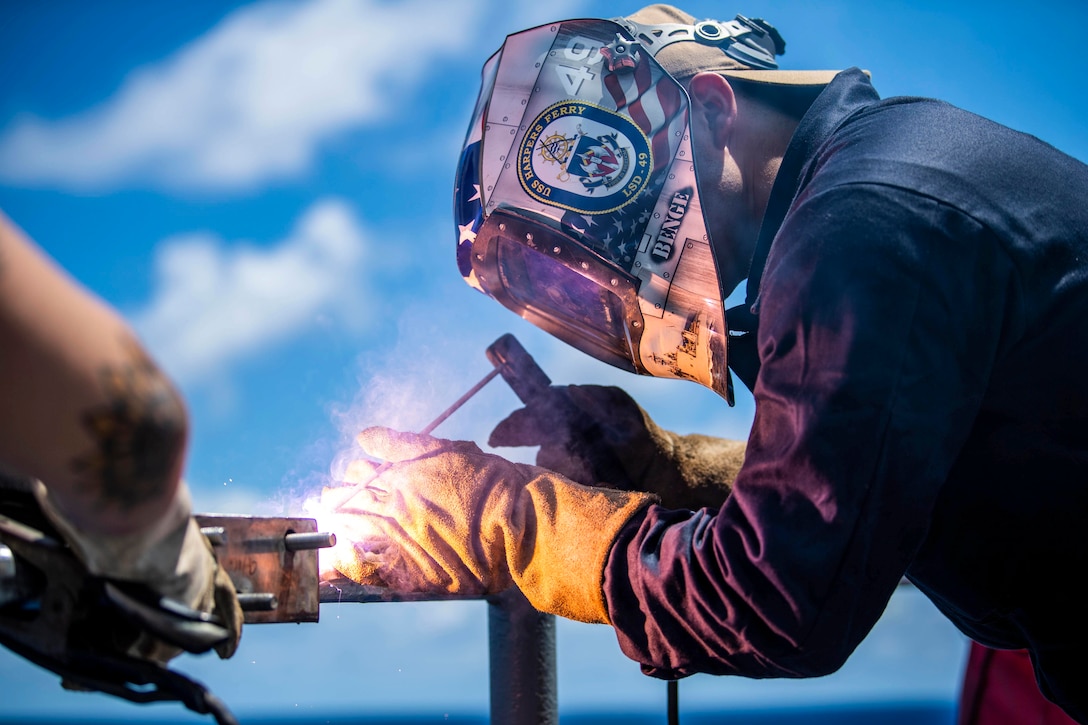 A sailor wearing a mask uses a tool to weld.