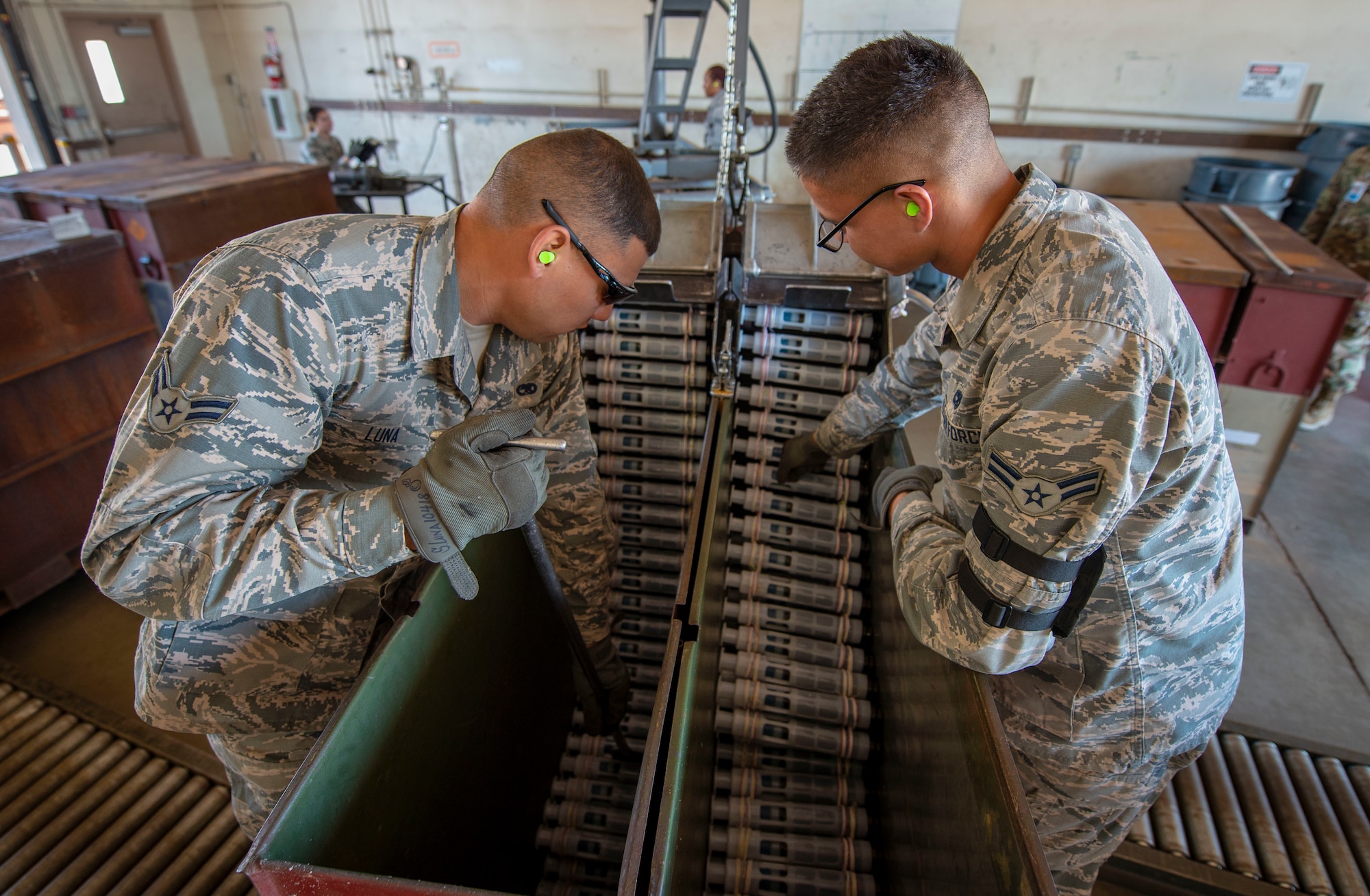 U.S. Air Force Airman 1st Class Stephen Luna, 57th Munitions Squadron (MUNS), small bombs crew member, and Airman 1st Class Christopher Conley, 57th MUNS small bombs crew chief, ensure the thread of 30mm round containers do not get jammed in the GFU-7 while being processed at Nellis Air Force Base, Nev., June 4, 2019. The machine processes the 30mm rounds by counting all serviceable and non-serviceable rounds as well as separating the brass from the ammunition downloaded from A-10 Thunderbolts and returns good rounds into another container. (U.S. Air Force photo by Staff Sgt. Tabatha McCarthy)