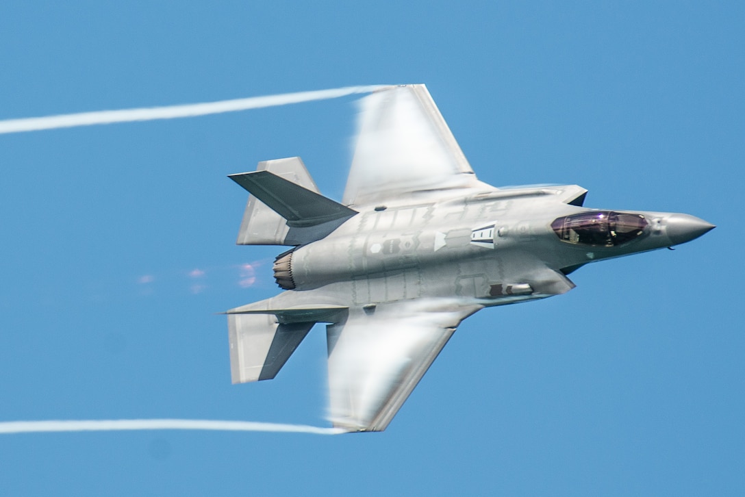 A fighter aircraft leaves trails from its wingtips against a blue sky.
