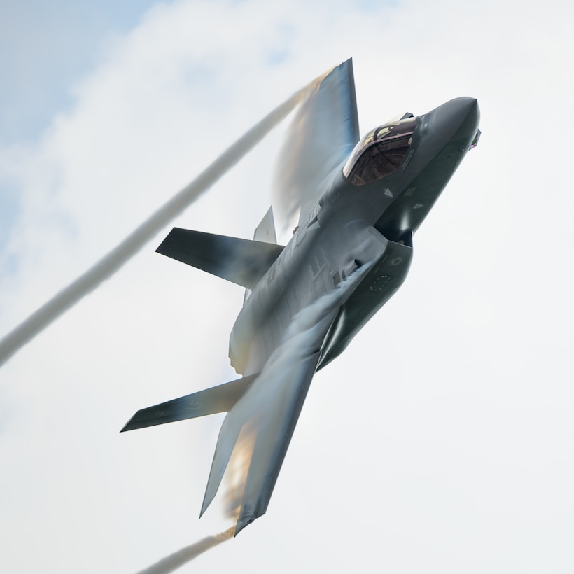 A fighter aircraft leaves trails from its wingtips against a backdrop of clouds.