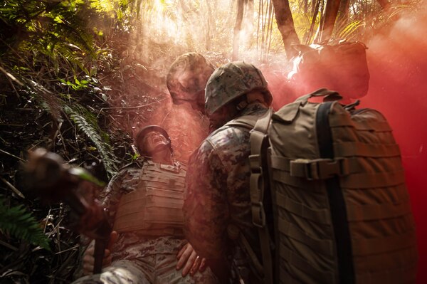 Sailors care for a fallen Sailor in red smoke.