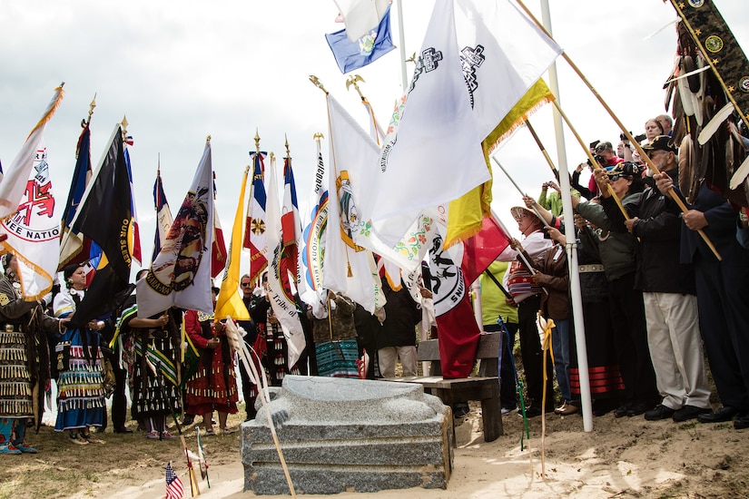 People hold flags at a memorial ceremony on Omaha Beach.