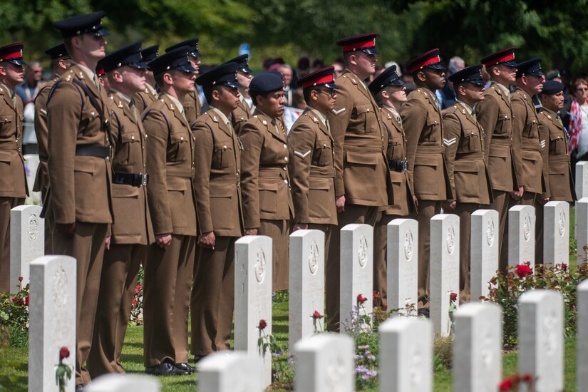 Soldiers in a line stand behind graves.