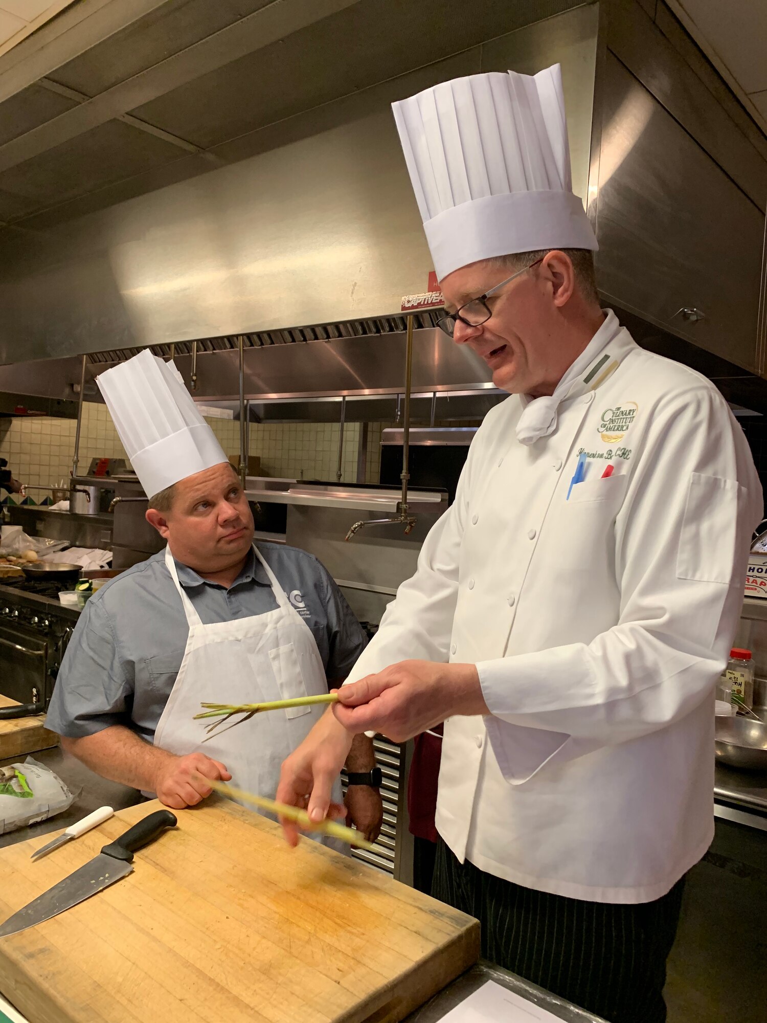 Culinary Institute of America Chef Hinnerk von Bargen demonstrates how to prepare lemon grass for chopping to cook Justin Lentz from Buckley Air Force Base, Colorado, during the practical portion of the new Air Force Techniques of Healthy Cooking Course at the CIA San Antonio campus, June 5, 2019. Lentz and 15 other nonappropriated fund employees from across the Air Force attended the course established by the Air Force Services Center, in partnership with the CIA San Antonio. The five-day course is designed to teach and demonstrate healthier ingredients, flavorful spicing and better cooking methods to deliver healthier menu choices at food service operations across installations, not just at dining facilities. (U.S. Air Force photo by Debbie Aragon)