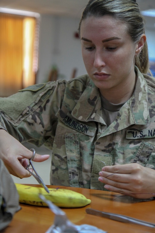 Master at Arms Seaman Kortni Amundson, military working dog handler with Area Support Group-Qatar, practices her suturing technique on a banana during a training on how to better treat military working dogs and provided by the 719th Medical Detachment Veterinary Service Support, May 31, 2019.