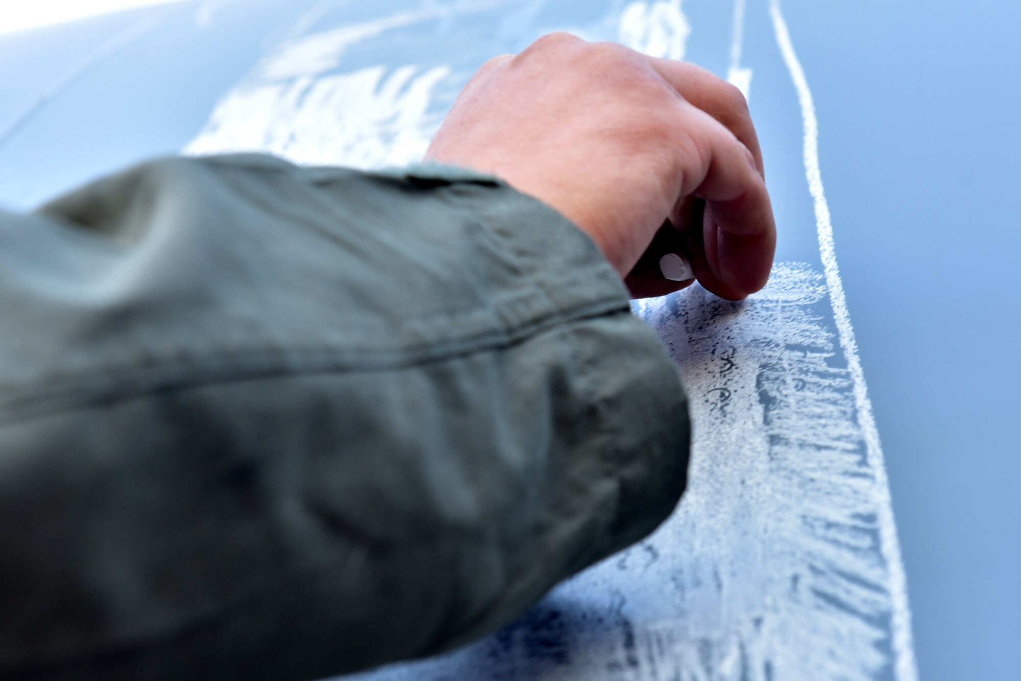 An Airman draws with chalk on the side of a C-130J
