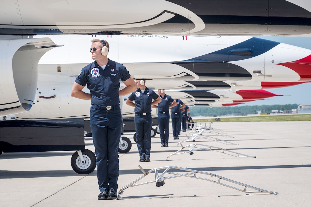 Members of the Thunderbirds, the Air Force's flight demonstration team, stand in a row next to aircraft.