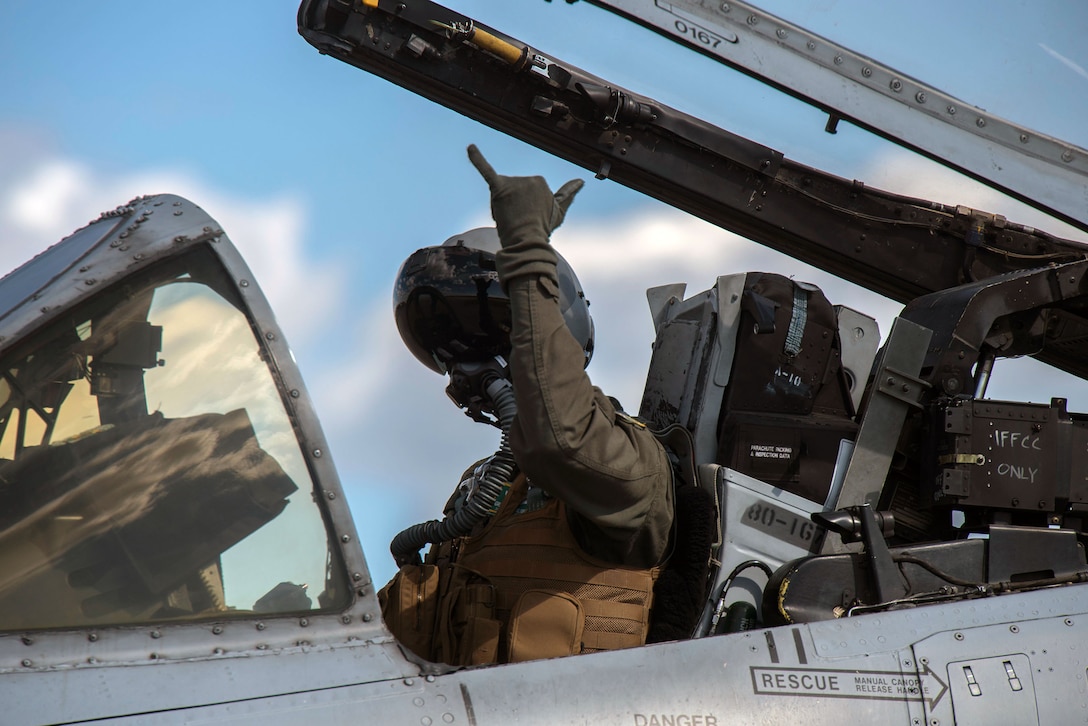 An Air Force pilot gives a hand signal while in an open cockpit.