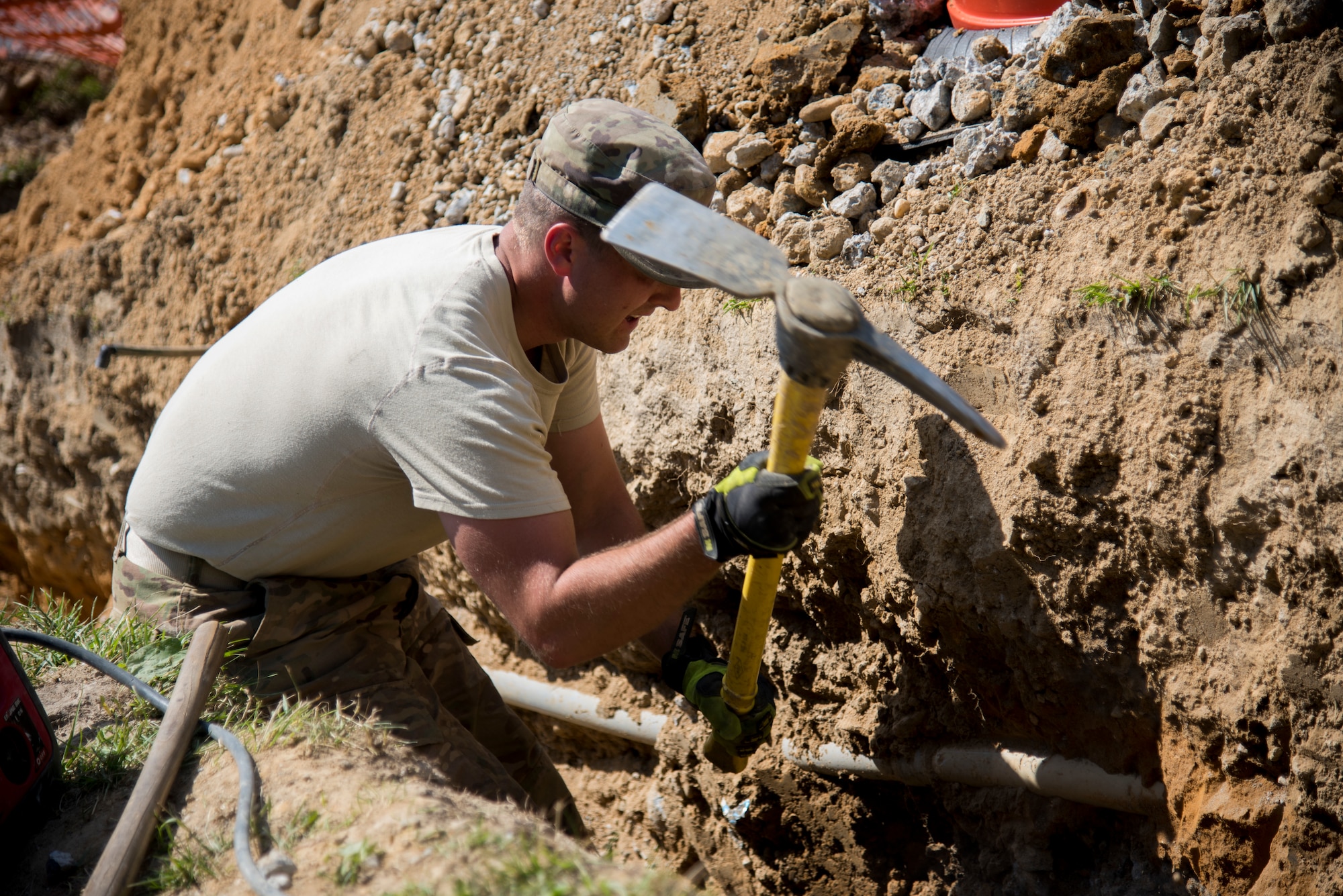 Staff Sgt. Logan Pals, 436th Civil Engineer
Squadron pavement and equipment craftsman,
uses a pickaxe to break down the walls of a
trench being dug near the main gate June 3,
2019, at Dover Air Force Base, Del. “Dirt Boyz”
are also responsible for upkeep of the roads on
base. (U.S. Air Force photo by Airman 1st Class
Jonathan Harding).