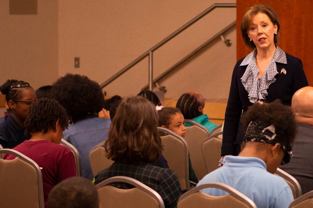 A woman speaks to children in an auditorium.