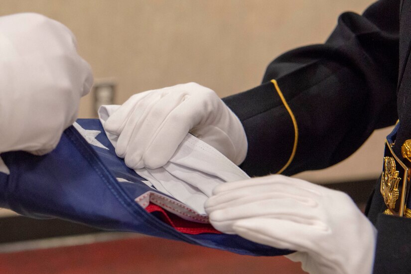 Service members wearing gloves fold an American flag.