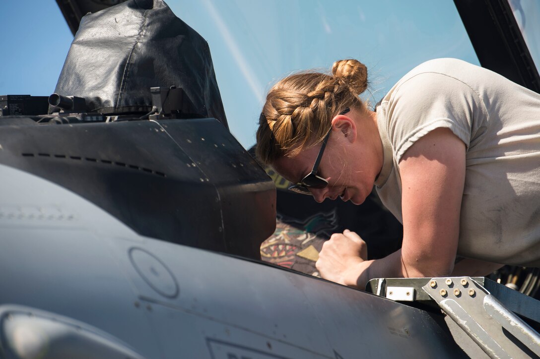 An airman peers into the cockpit of a fighter jet to see if adjustments should be made.