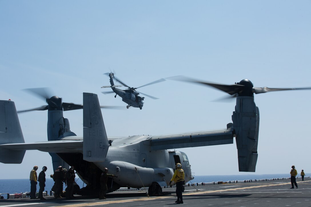 An MH-60S Seahawk takes off as Marines and Sailors with the 31st Marine Expeditionary Unit and the amphibious assault ship USS Wasp (LHD 1) unload supplies from an MV-22B Osprey tiltrotor aircraft while underway in the Philippine Sea, June 5, 2019. The 31st Marine Expeditionary Unit, the Marine Corps` only continuously forward-deployed MEU, provides a flexible and lethal force ready to perform a wide range of military operations as the premier crisis response force in the Indo-Pacific region. (Official U.S. Marine Corps photo by Lance Cpl. Kenny Nunez Bigay)