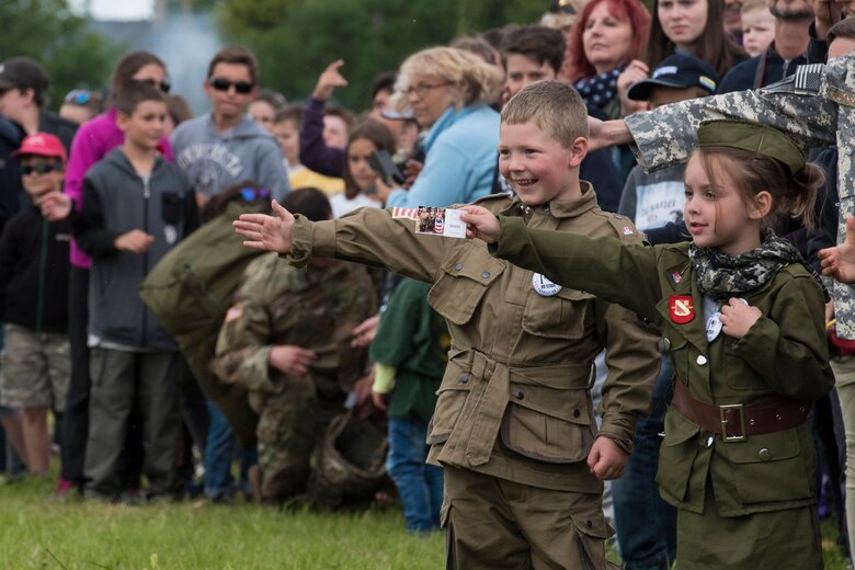 A French boy, dressed in a mock WWII-era uniform displaying the American flag, Canadian flag and an illustrated pin stating “I heart our veterans,” extends his arm waiting to high five one of the many U.S. static-line paratroopers walking by during the D-Day 75 Commemorative Airborne Operation outside of Sainte-Mère-Église, France, June 9, 2019. Next to him, a French girl, extends her hand to give the paratroopers a token of gratitude which says “Thank You,” in four different languages. Thousands of spectators showed up for the multinational commemorative events to witness an airshow and 900 paratroopers descend from the skies into the Iron Mike drop-zone, commemorating D-Day, 75 years ago. (U.S. Air Force photo by Senior Airman Kristof J. Rixmann)