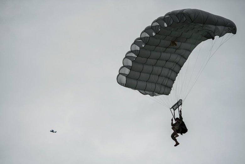 A military-free-fall paratrooper lands as a United States Air Force CV-22 Osprey, assigned to the 352nd Special Operations Wing flies above the Iron Mike Drop Zone outside of Saint-Mere-Eglise, France June 9, 2019. Iron Mike Drop Zone is a historic location to Operation Overlord. (U.S. Air Force photo by Senior Airman Devin M. Rumbaugh)