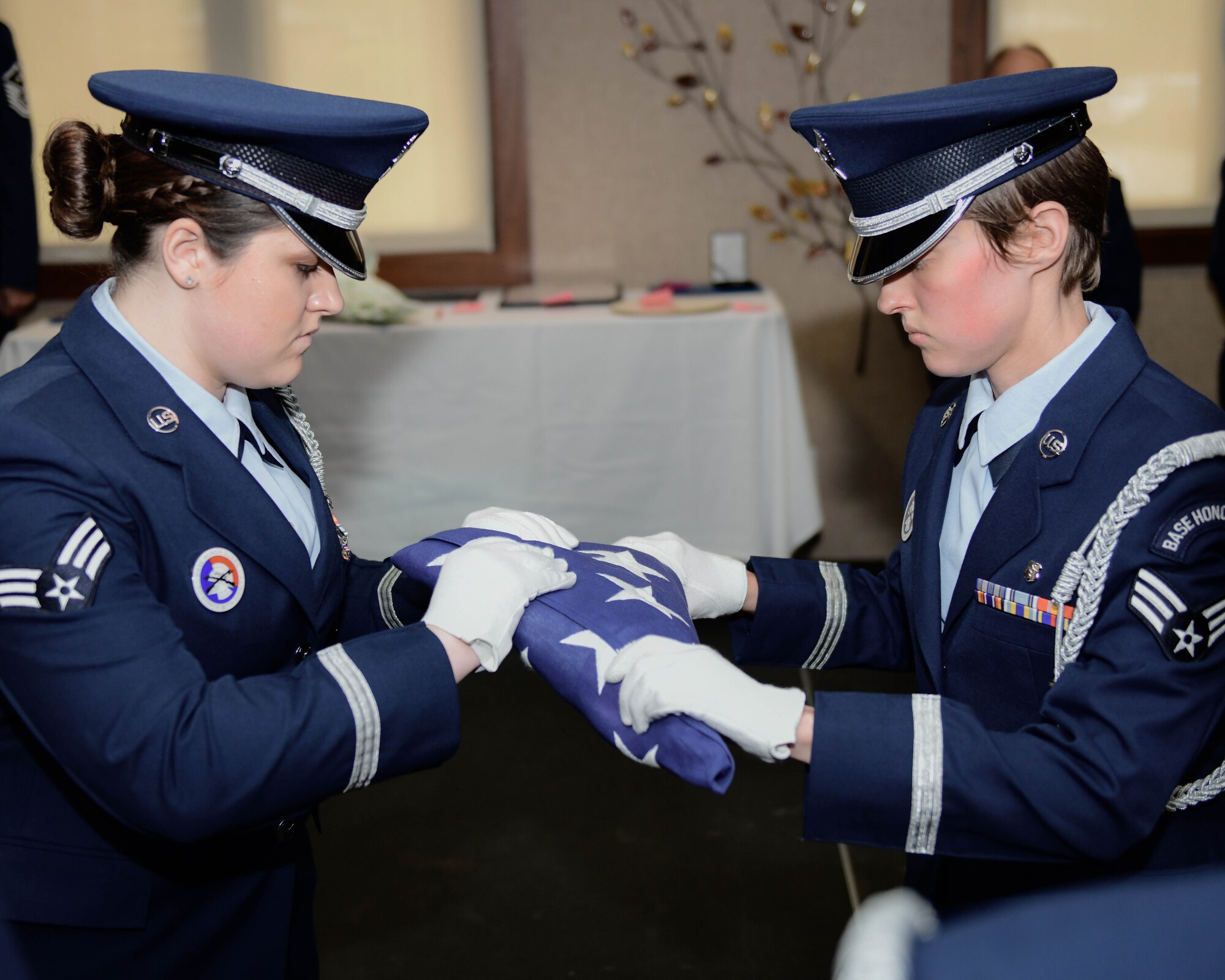 Senior Airman Marjorie Butcher and Senior Airman Emma German, both aerospace medical services technicians with the 910th Medical Squadron, take part in a United States flag presentation during a retirement ceremony for Col. Rodeny Waite, the commander of the 910th MDS, May 4, 2019.