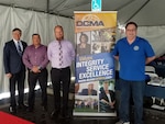 Four men stand in front of a tall D. C. M. A. sign.