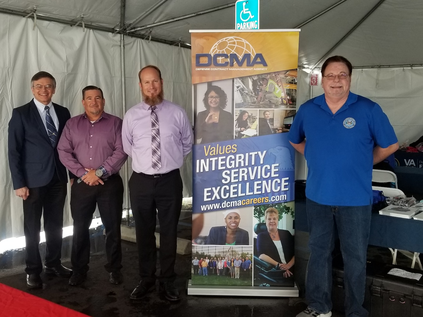 Four men stand in front of a tall D. C. M. A. sign.