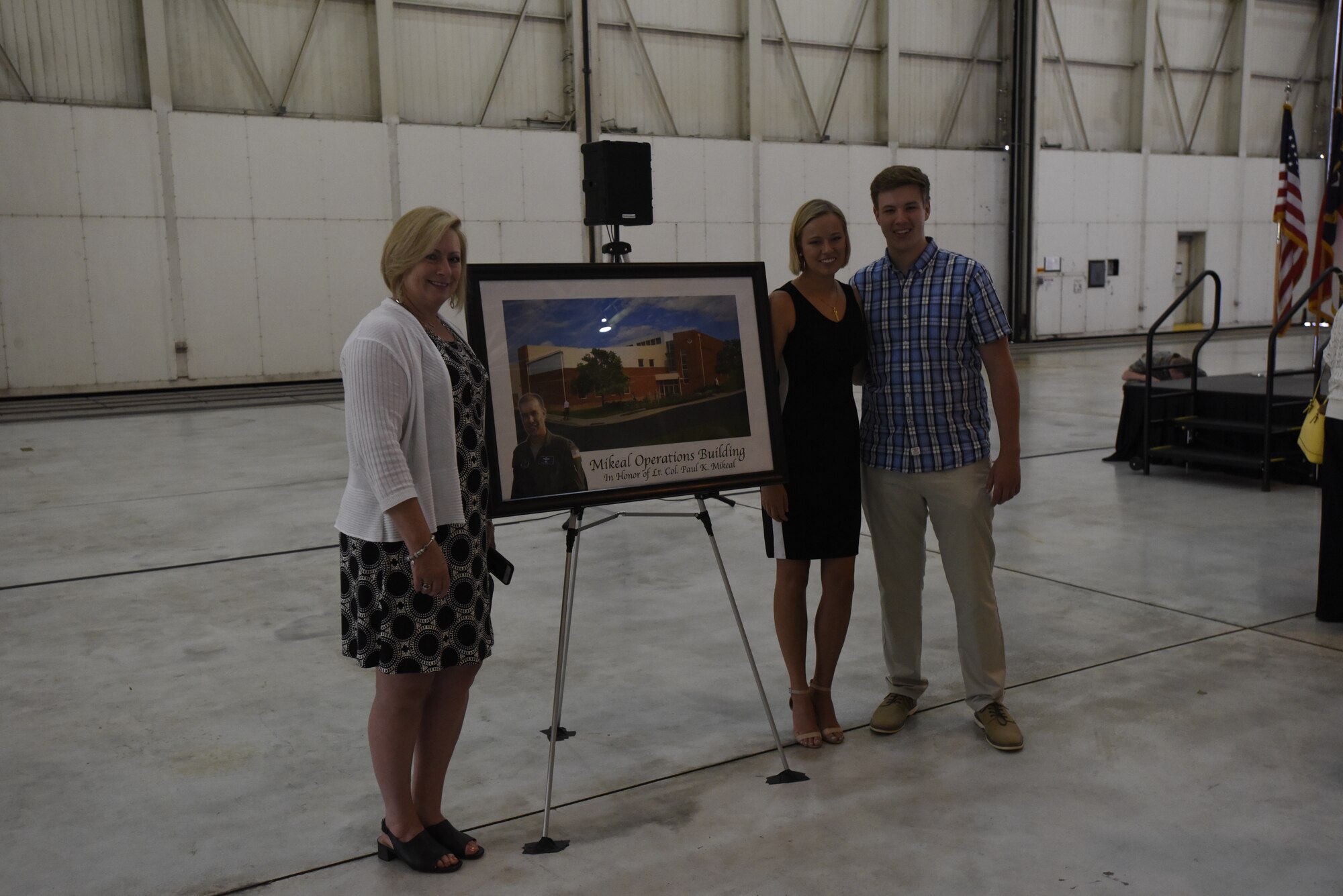 The family of U.S. Air Force Lt. Col. Joseph Mikeal pose next to a commemorative photo created for the 145th Airlift Wing building dedication ceremony at the North Carolina Air National Guard Base, Charlotte Douglas International Airport, June 9, 2019. Lt. Col. Mikeal was a member of the MAFFS 7 crew who passed away in an aircraft accident in 2012, the 145th Airlift Wing honored his and the other crew members sacrifice by naming four buildings across the wing after each one.