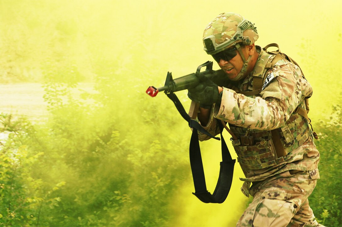 An airman runs through yellow smoke with a weapon.