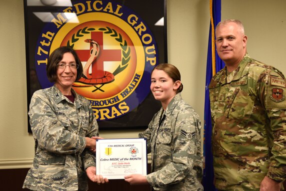 U.S. Air Force Col. Janet Urbanski, 17th Medical Group commander, presents Airman 1st Class Jade Herb, 17th MDG mental health technician, with the Medic of the Month award with Chief Master Sgt. Matthew Moore, 17th MDG superintendent. The Medic of the Month is presented to members of the 17th Medical Group who exceed expectations and show outstanding Airmanship. (U.S. Air Force photo by Senior Airman Seraiah Hines/Released)