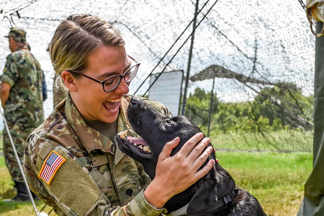 A smiling soldier pets a smiling dog.
