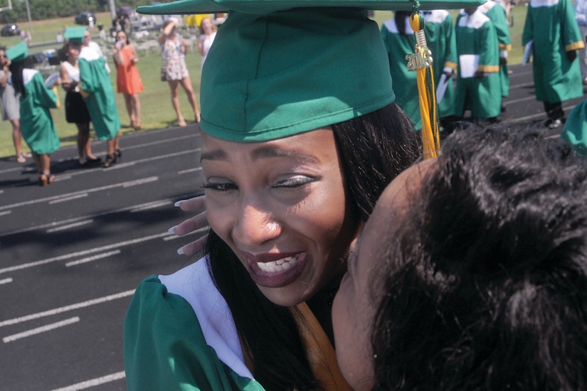 A young woman in a cap and gown hugs a woman at a graduation.