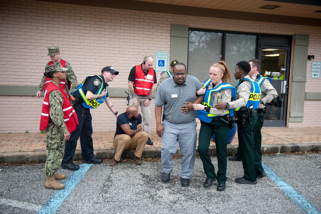 Civilian first responders wearing reflective vests help a role-player as military personnel look on.