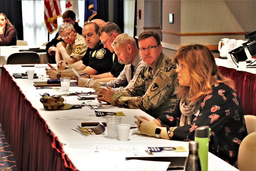 Military and civilian personnel hold a meeting at a table.