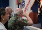 Two men salute the US flag. Woman in background.