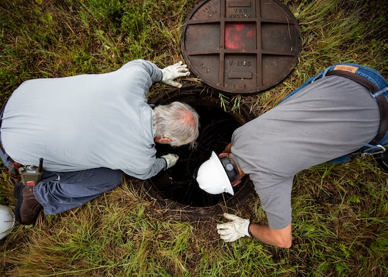 Frank Cutchens and John Dunham, J&J Worldwide Services base operations personnel, search for primary electric lines in a manhole June 6, 2019, on the flightline at Tyndall Air Force Base, Florida. J&J Worldwide Services provides Tyndall with multiple services including utilities infrastructure services, heavy equipment services, grounds maintenance, pest control and more. (U.S. Air Force photo by Airman 1st Class Bailee A. Darbasie)