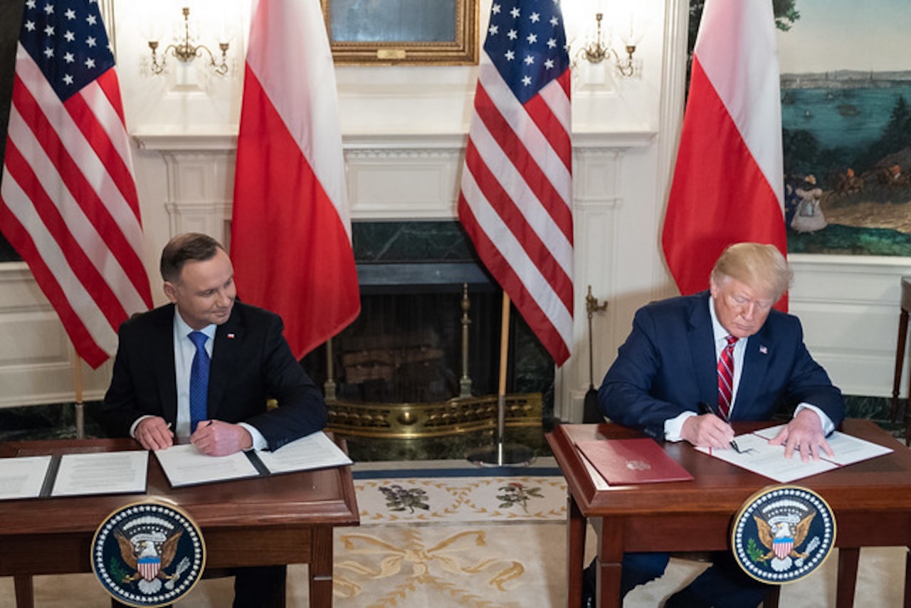 President Donald J. Trump and Polish President sit at two tables signing documents.