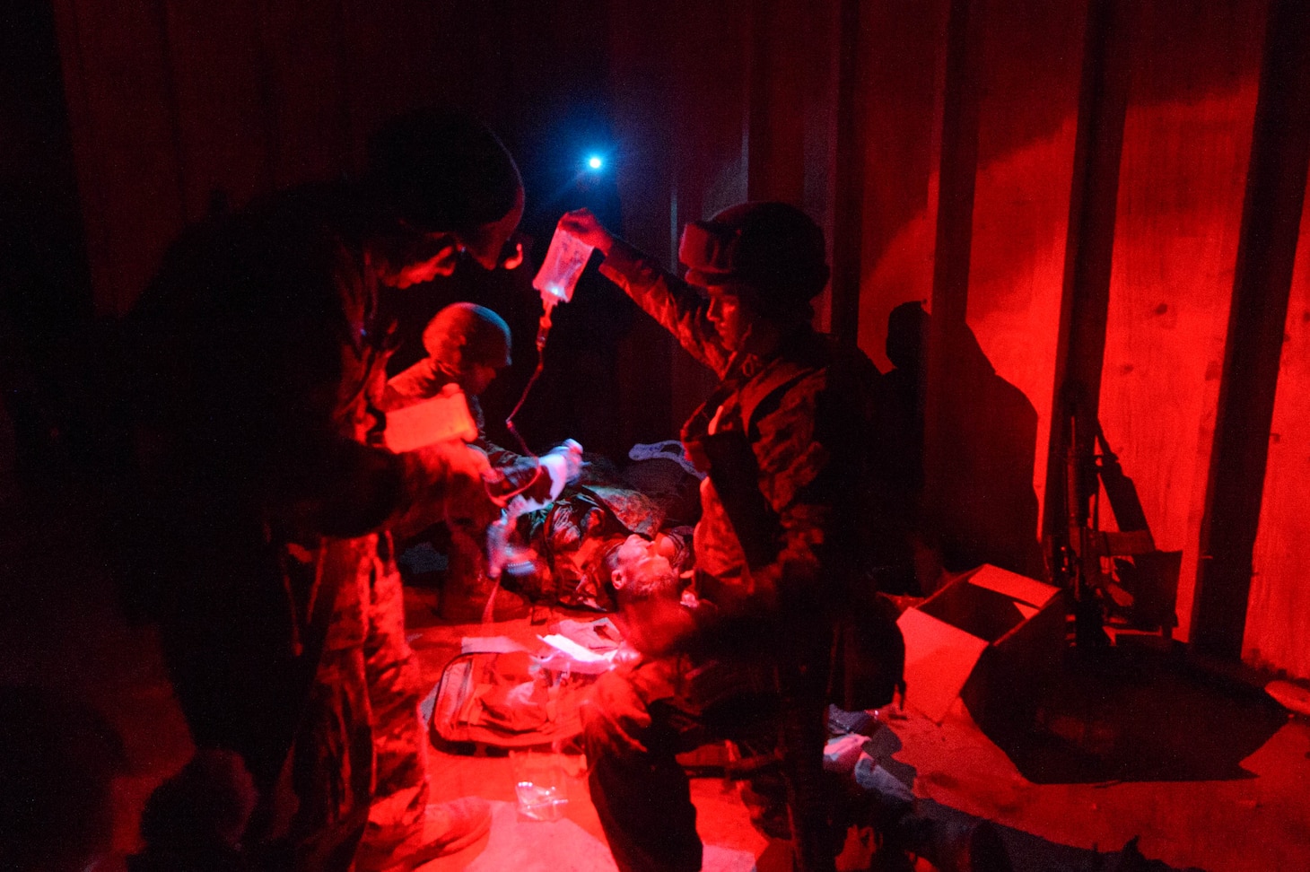 Sailors administer medical care to a mannequin in red light.