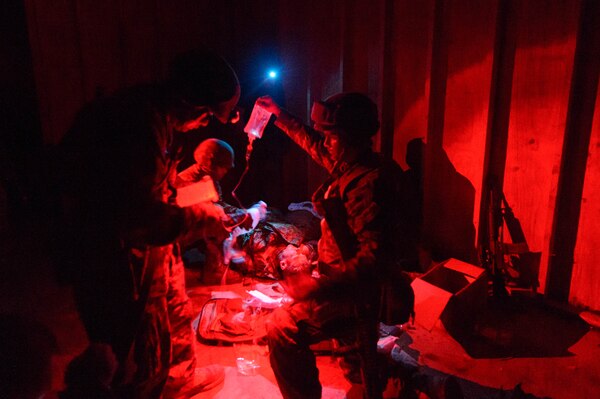 Sailors administer medical care to a mannequin in red light.