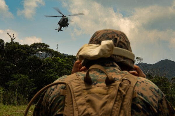 A sailor stands in front of a landing helicopter.