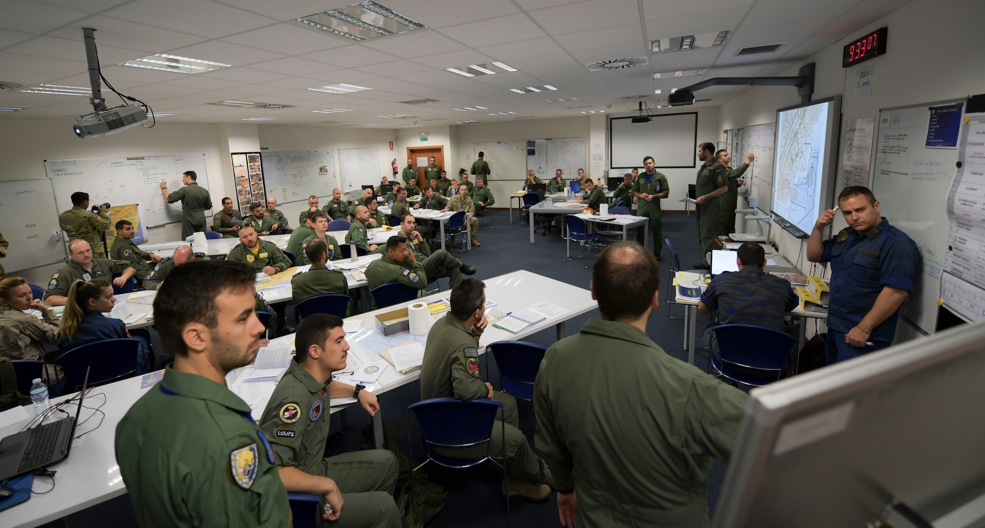 Group of U.S. and NATO pilots seen in pre-flight briefing room.