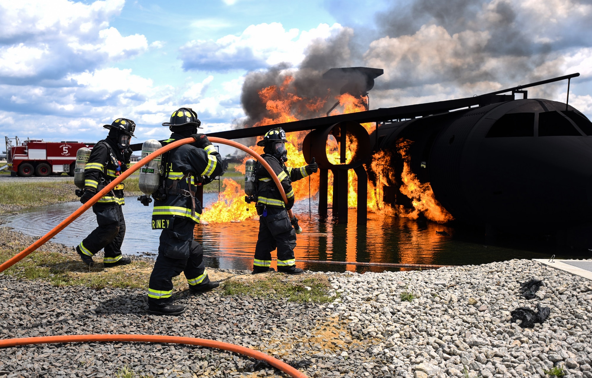 Fire fighters with the 87th Civil Engineer Squadron fire department prepare to put out a burning model aircraft during fire training on Joint Base McGuire-Dix-Lakehurst, New Jersey, June 3, 2019. The Fire training is used for Airmen completing their career development courses and for fire fighters to practice their skills in putting fires out while dealing with different weather elements. (U.S. Air Force photo by Airman 1st Class Ariel Owings)