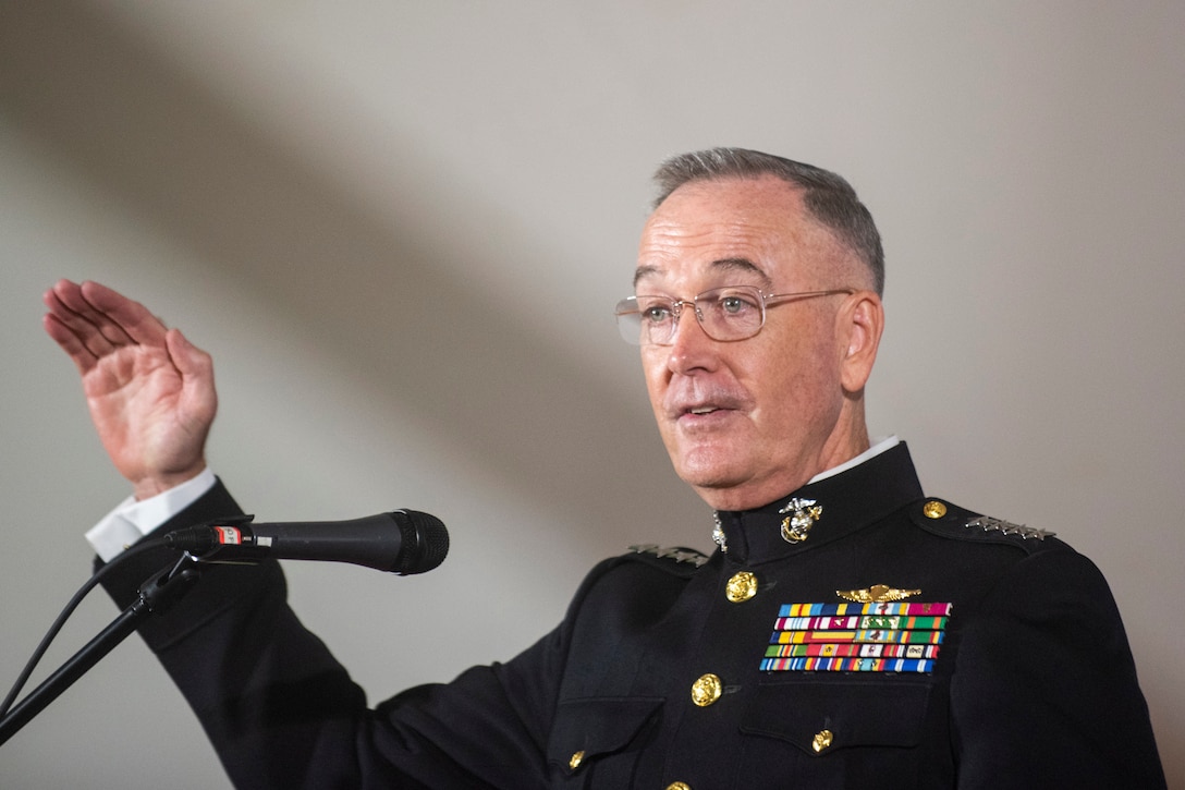 A general raises his hand while standing and speaking into a microphone.