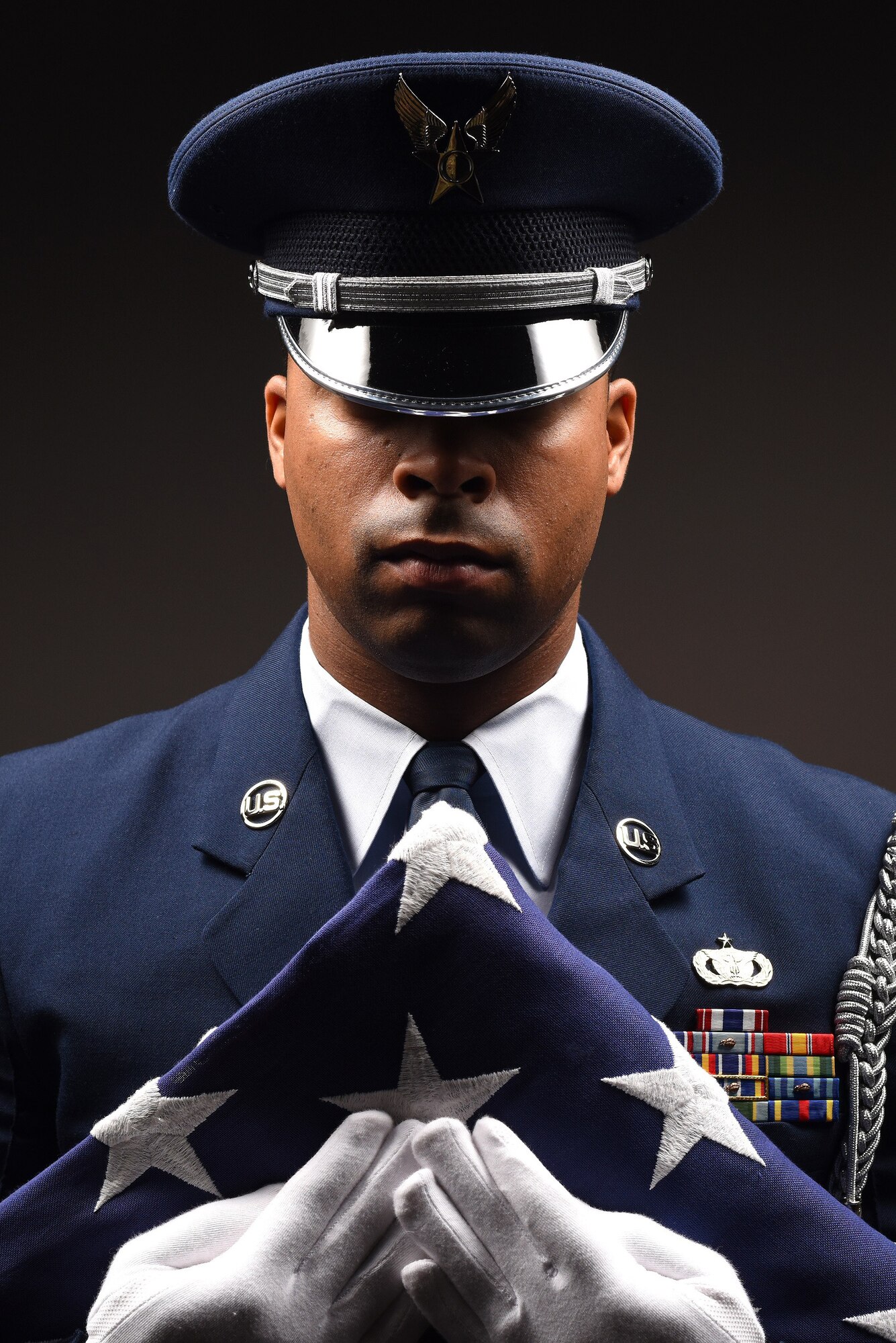 Staff Sgt. Alonzo Clark, 319th Air Base Wing Honor Guard program manager, grips a folded flag of the United States of America to his chest June 5, 2019, on Grand Forks Air Force Base, North Dakota. Clark manages the small, eight-person team of airmen on base, which has regional responsibility of 153,000 square-miles, to include North Dakota, Minnesota, Michigan and Wisconsin. Becoming a guardsman is an earned position of honor and duty, reserved only for members who strive to preserve the U.S. Air Force heritage. (U.S. Air Force photo illustration by Senior Airman Elora J. Martinez)