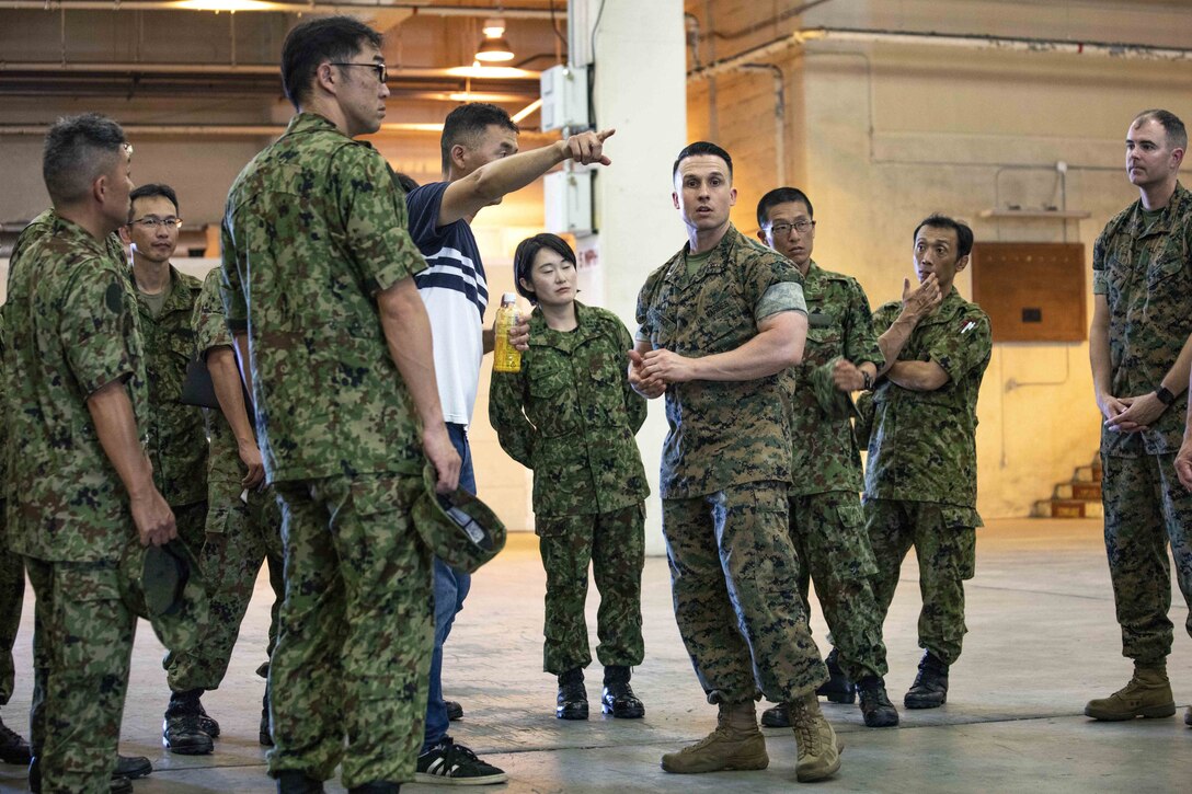 Japanese translator and administrative specialist, Kensuke Kobayashi, translates for U.S. Marine Corps Chief Warrant Officer 3 Alan Thompson during a community exchange program tour with the Japanese Ground Self-Defense Force on Camp Kinser, Okinawa, Japan June 7, 2019. During the tour, hosted by Combat Logistics Regiment 35, service members visited the base dining facility, supply management unit, a maintenance shop, and the Battle of Okinawa historical display, before taking part in a social at the USO. The purpose of the program is to create bonds and increase operational understanding between the JGSDF and the U.S. Marine Corps. Kobayashi, is a native to Fukuoka, Japan. Thompson, the Supply Management Unit operations officer, CLR-35, 3rd Marine Logistics Group, is a native of Charleston, West Virginia. (U.S. Marine Corps photo by Pfc. Courtney A. Robertson)