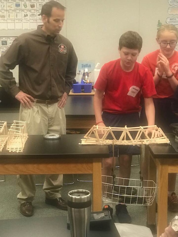 Transatlantic Middle East District's civil engineer Ted Upson assists students with the weight bearing test following their bridge build project at the STARBASE Academy Winchester.
